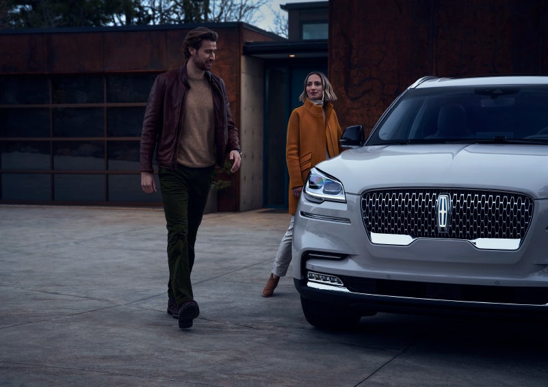 A man and a woman approaching a 2024 Lincoln Aviator® SUV, which illuminates certain lights when they are close | Sentry Lincoln in Medford MA