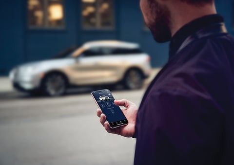 A person is shown interacting with a smartphone to connect to a Lincoln vehicle across the street. | Sentry Lincoln in Medford MA